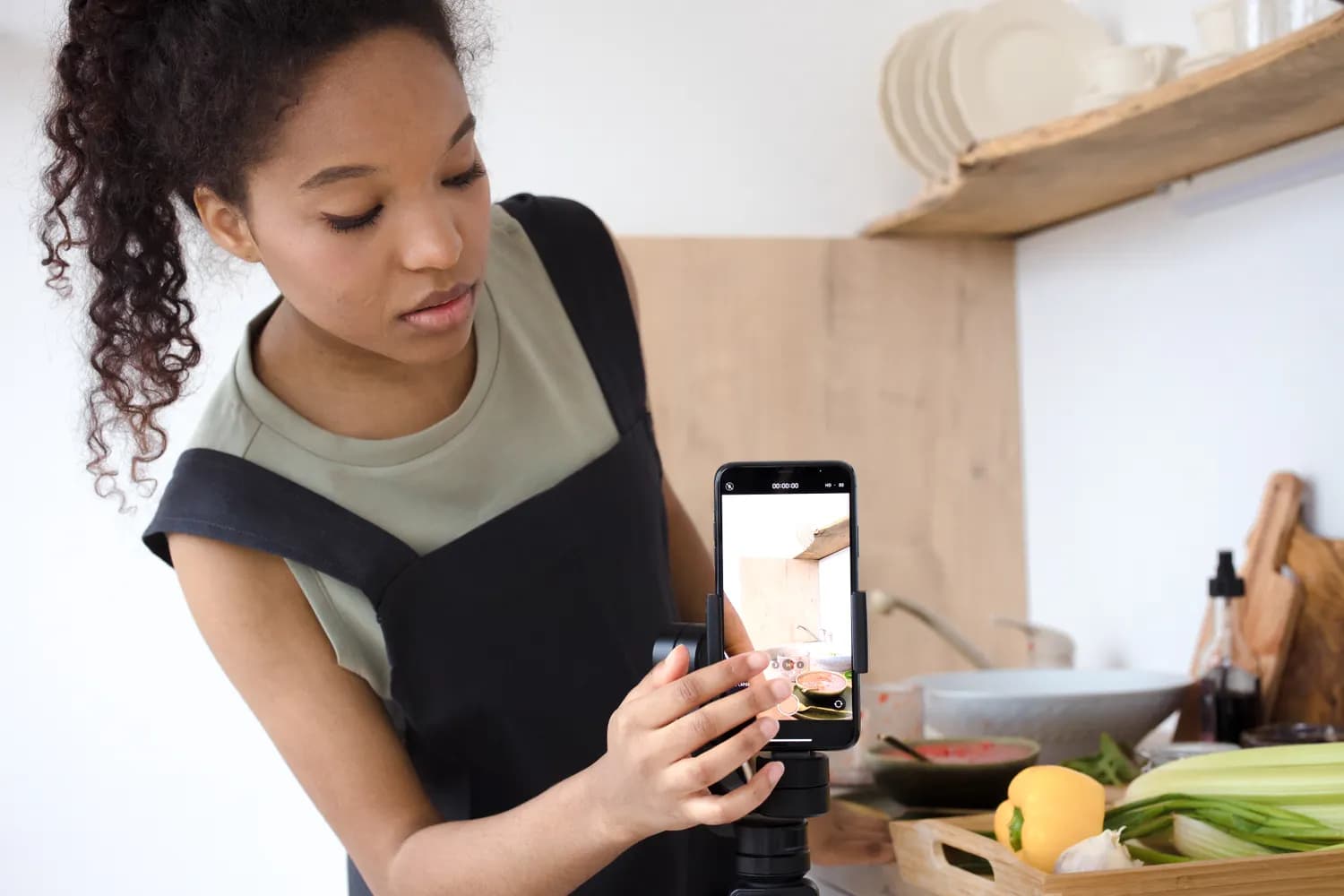 Une femme filme un plat au smartphone monté sur trépied, dans la cuisine où elle vient de le préparer