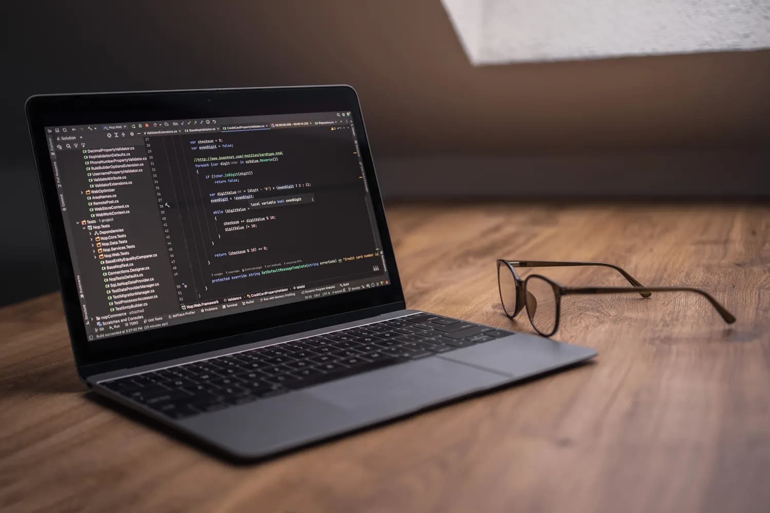 Un ordinateur portable ouvert sur un éditeur de code, posé sur un bureau en bois à côté d'une paire de lunettes