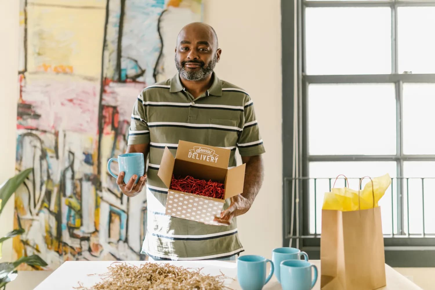 Un commerçant emballe des tasses bleues dans un carton d'expédition, sur la table de son atelier