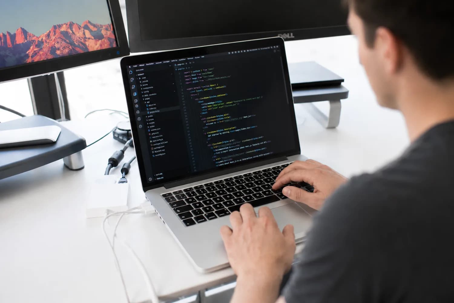 Un développeur code sur son ordinateur portable, entouré de deux écrans externes